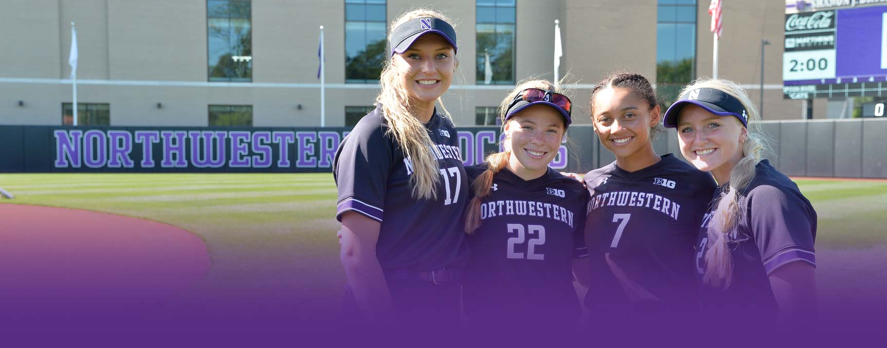Four softball players posing for a group photo on the field